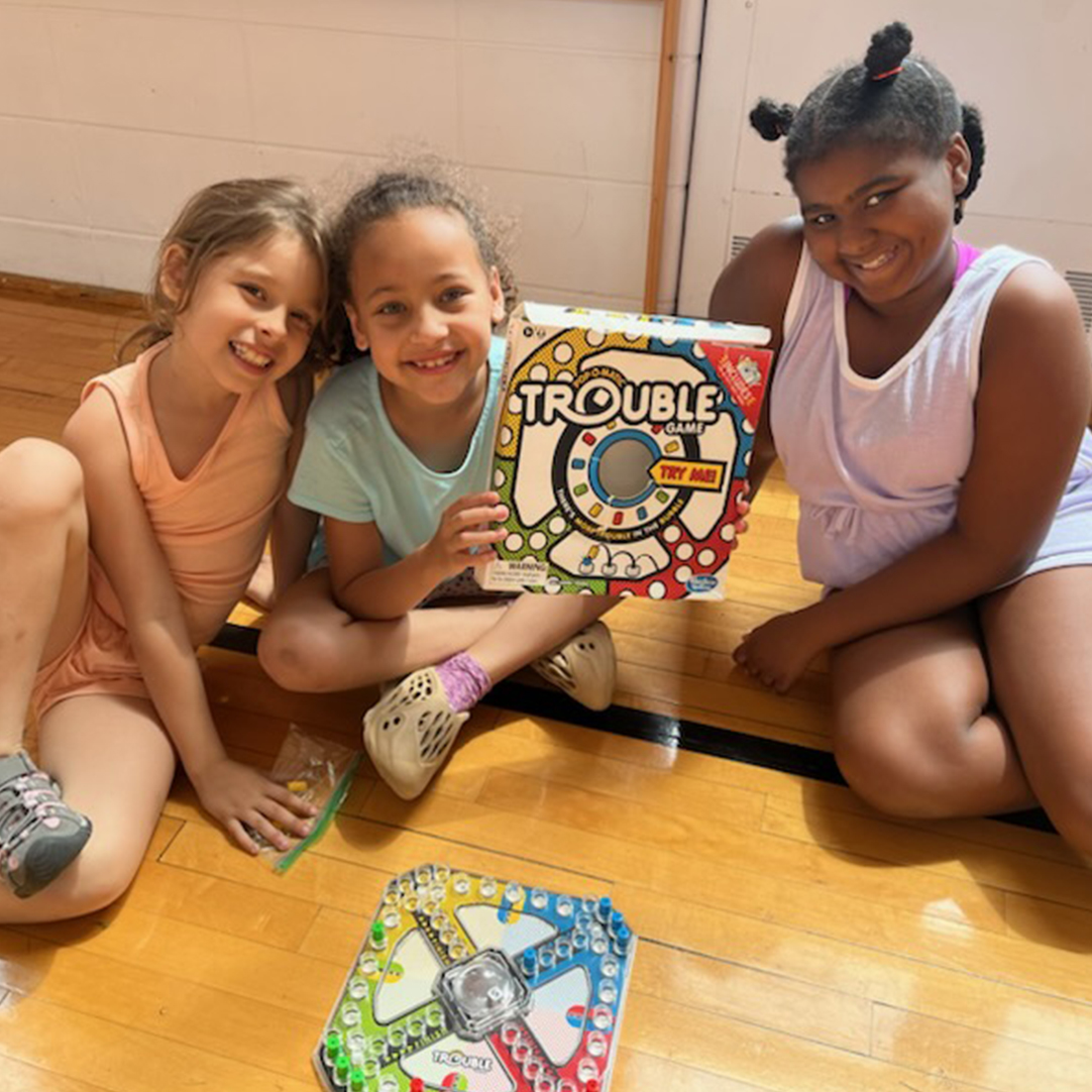 Three girls sitting on the floor with the board game "Trouble."