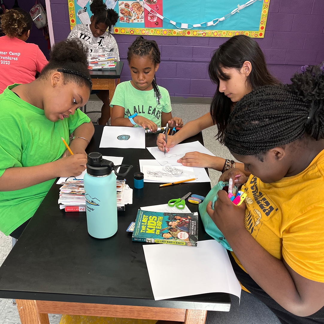 A group of students sitting at a table working on school work in a classroom.