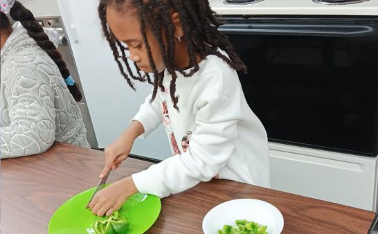 A child cutting a green bell pepper in a kitchen.