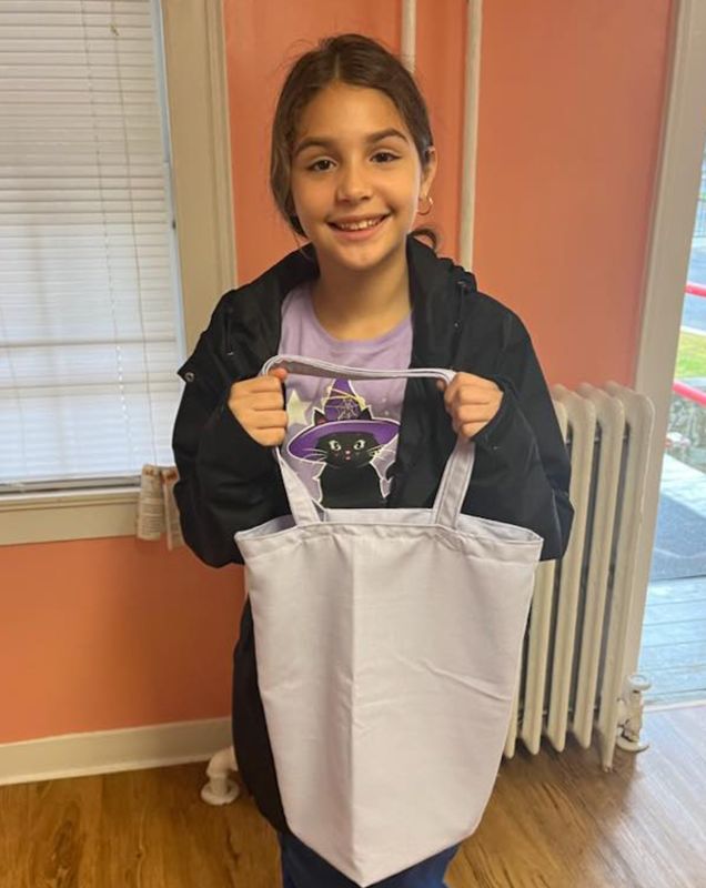A girl holding up a purple bag she made. 