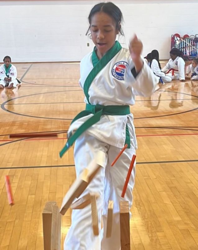 A girl in a karate class breaking a board with a front kick.